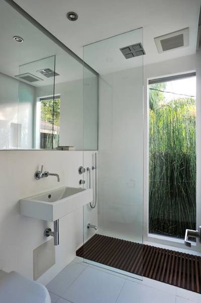 Salle de bains aux murs et au sol blancs, avec un miroir couvrant tout le mur.